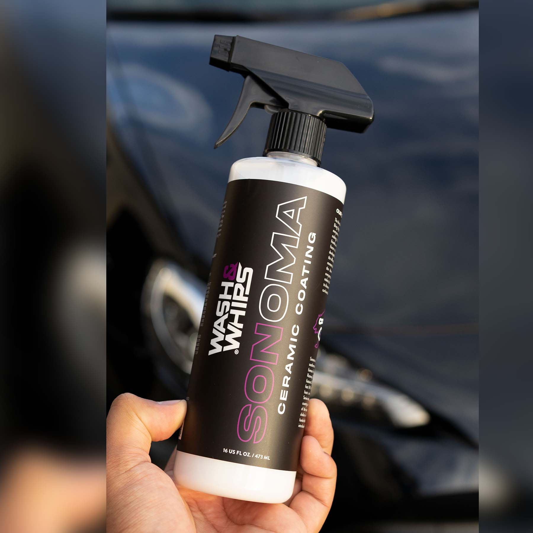 Hand holding a bottle of 'Wash & Wax Sonoma' ceramic coating in front of a car.