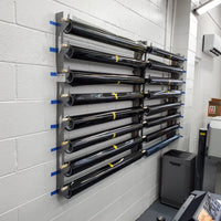 "Organized wall-mounted vinyl wrap rack in a professional print shop, featuring multiple levels of labeled tubes with black vinyl rolls, each marked with yellow stickers. This storage solution is set against a grey cinder block wall, optimizing the use of space in a busy working area."